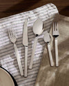 Modern silver stainless steel cutlery set by Alessi, with flat handles, on striped and textured napkins.