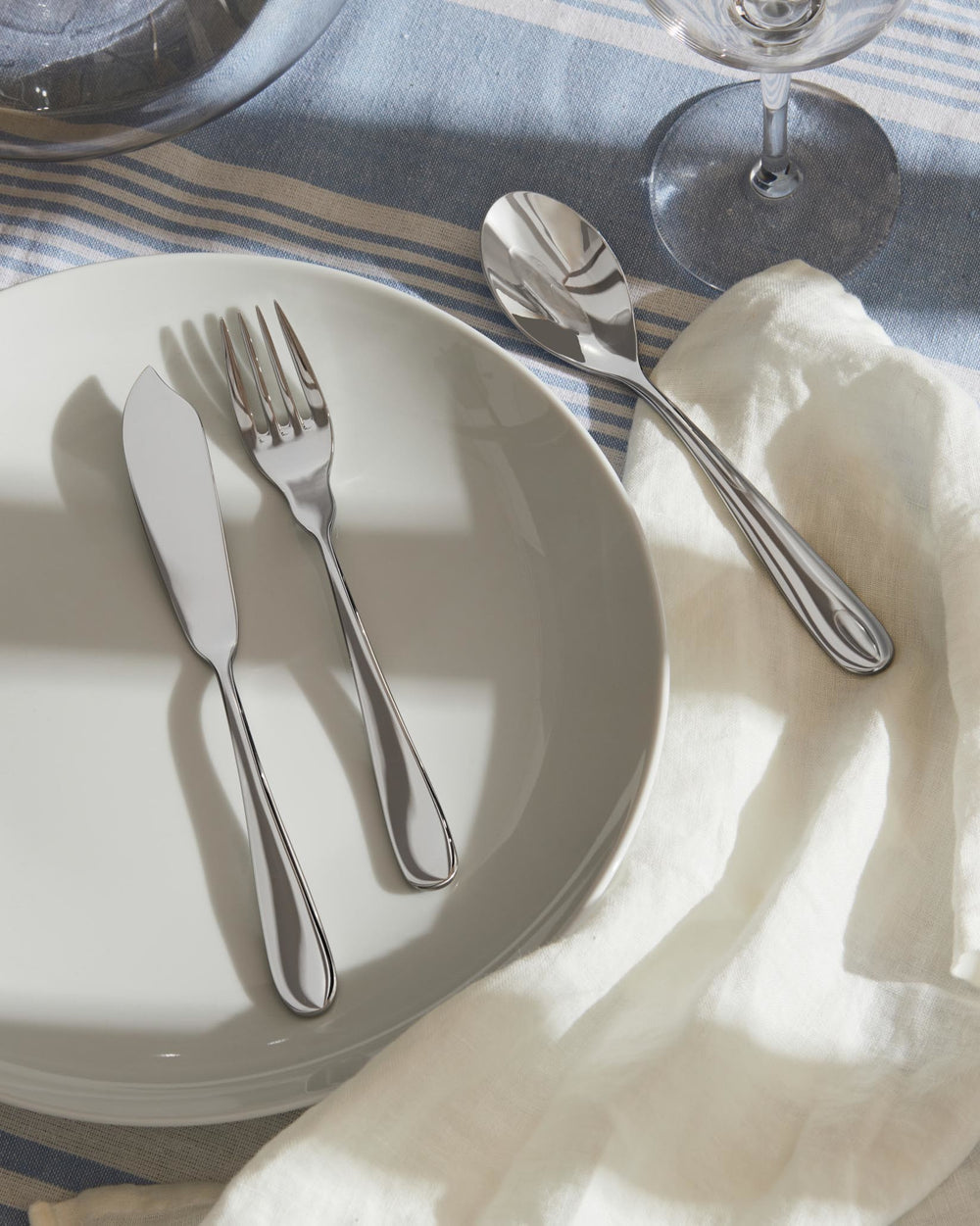 Silver polished cutlery set by Alessi, including a knife, fork, and spoon on a white plate.