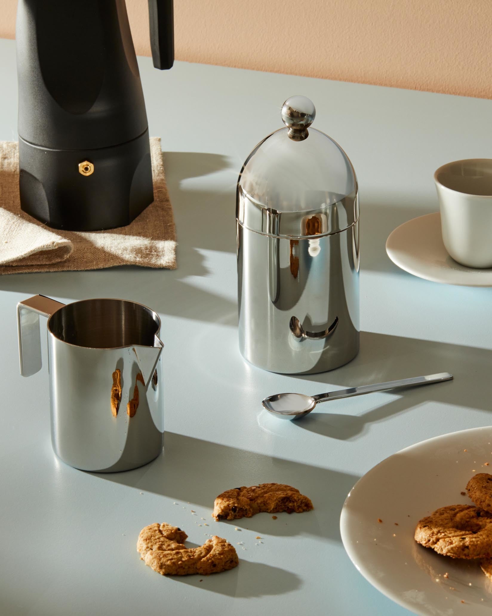 Polished stainless steel creamer by Alessi, with a sleek C-shaped handle and subtle spout.