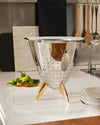 Polished stainless steel colander by Alessi with smiling bug perforations and three golden feet.