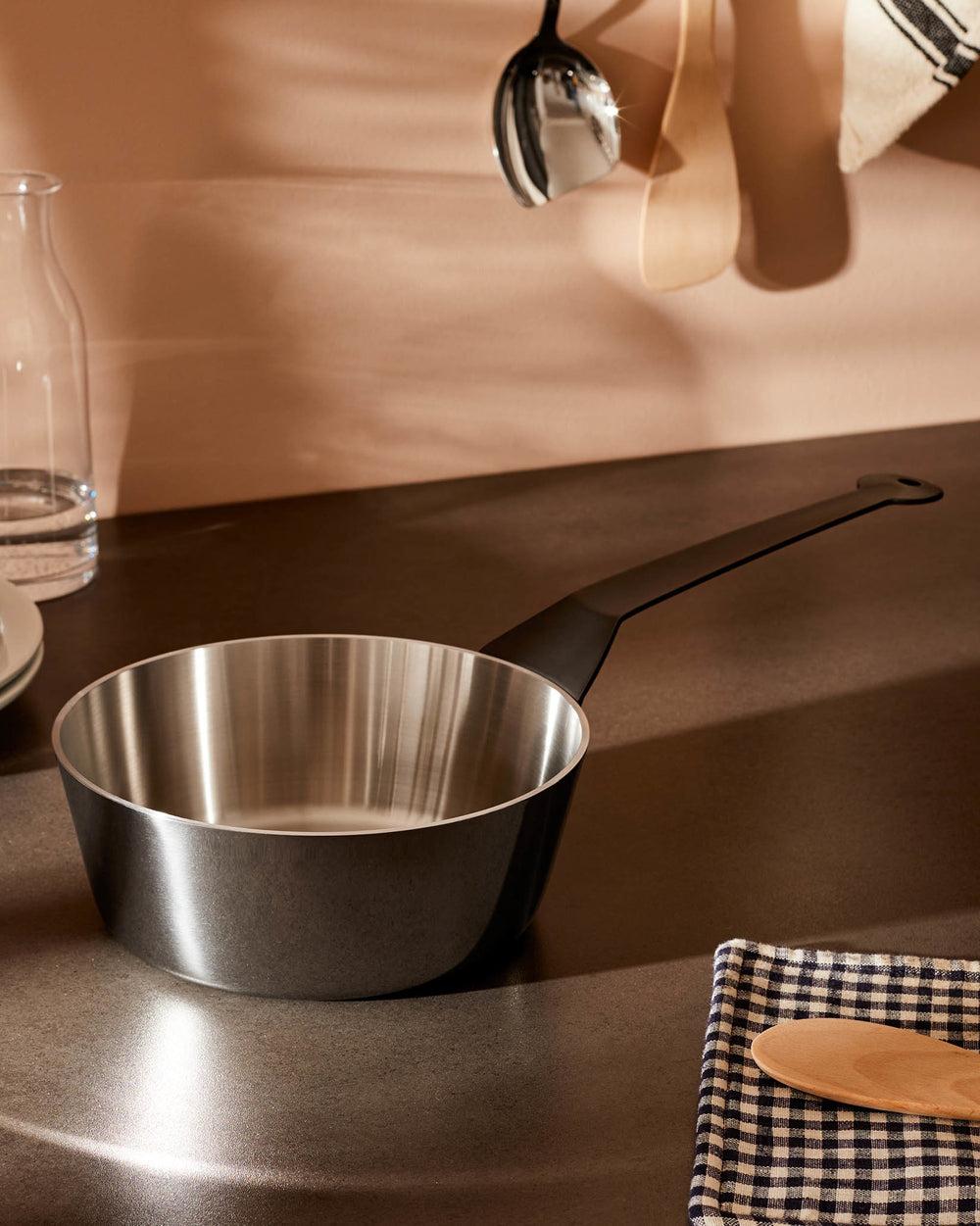 Dark grey saucepan with a polished stainless steel interior by Alessi, featuring a long black handle on a countertop.