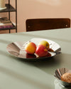 Silver stainless steel fruit bowl by Alessi, featuring a sculptural, pleated design, holding three apples on a light green table.