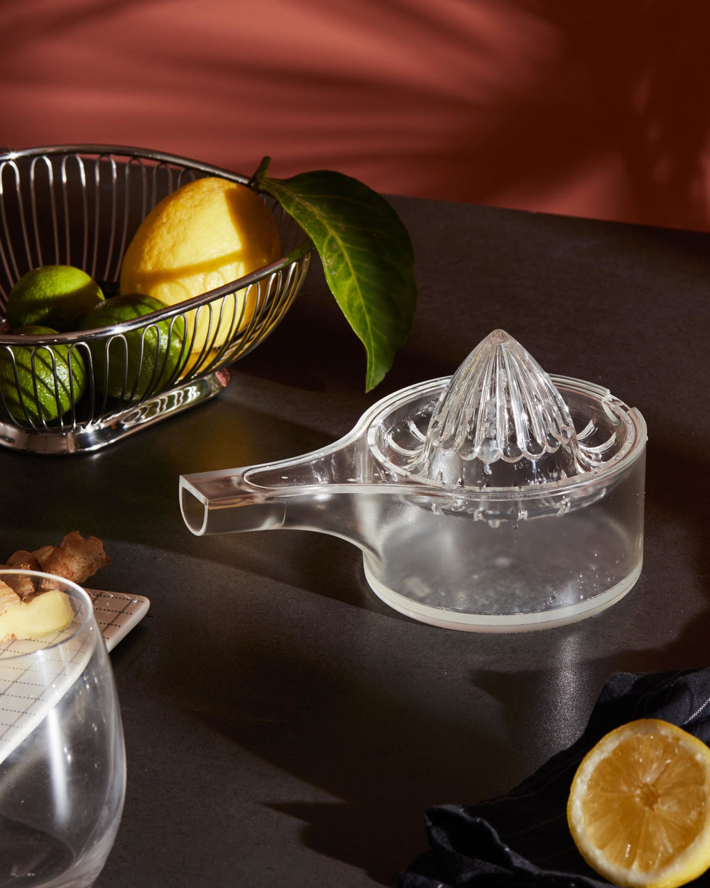 Clear plastic citrus squeezer by Alessi with a fluted reamer and pour spout, next to fresh lemons and ginger.