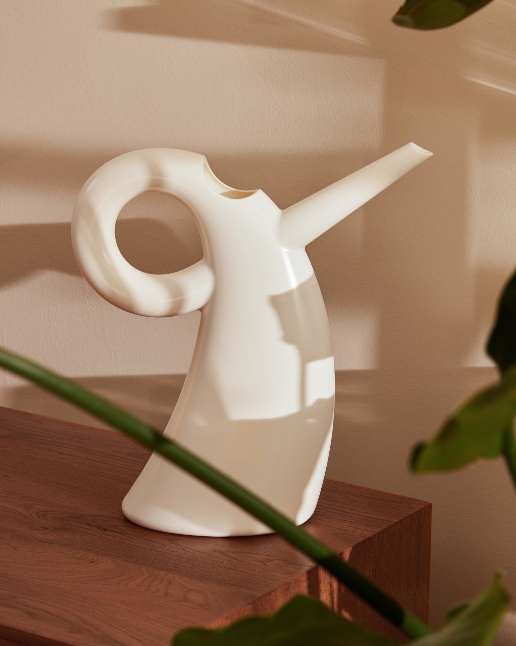 White Diva watering can by Alessi with a large circular handle, on a wooden surface.