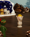 White ceramic Angelo Miracolo figurine by Alessi, with a yellow head and hands framing a smiling pink face.