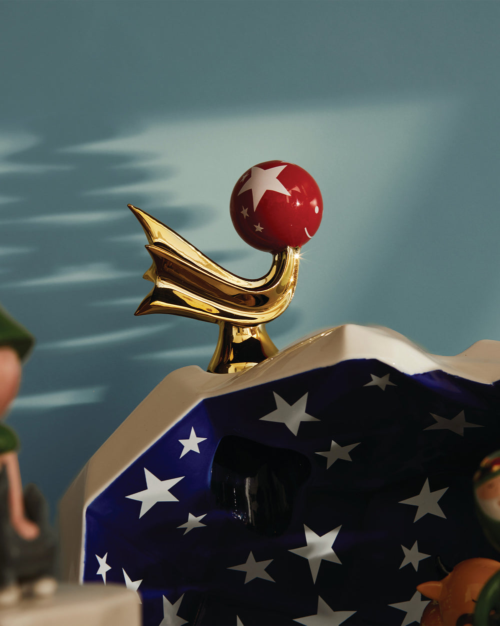 Gold Stella Cometa decorative object by Alessi, featuring a red star-patterned sphere and a blue starry base.