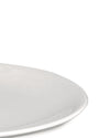 White, smooth plate by Alessi, shown in a cropped close-up with a curved rim.