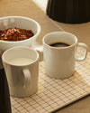 White rectangular serving tray by Alessi, with a black dotted grid pattern, holding two white mugs and a cereal bowl.