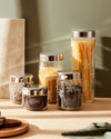 Clear glass storage jars by Alessi with silver lids, featuring the iconic 'Girotondo' pattern, filled with dry goods.