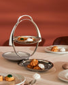 Foldable silver metal tiered serving stand by Alessi, displaying assorted cookies and meringues.