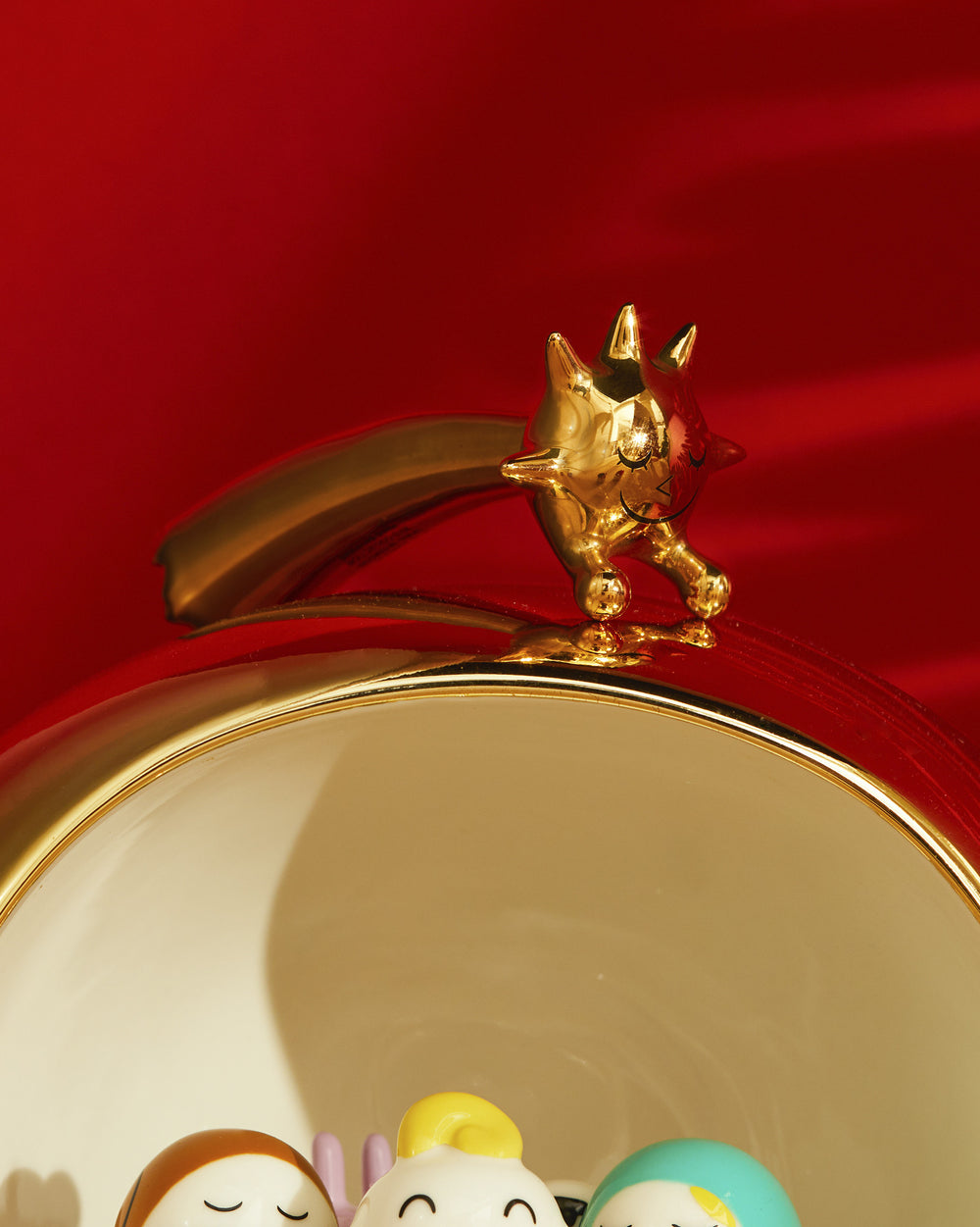 Golden star-shaped decorative object by Alessi, with a smiling face, perched on a red and gold-rimmed cup containing colorful figurines.