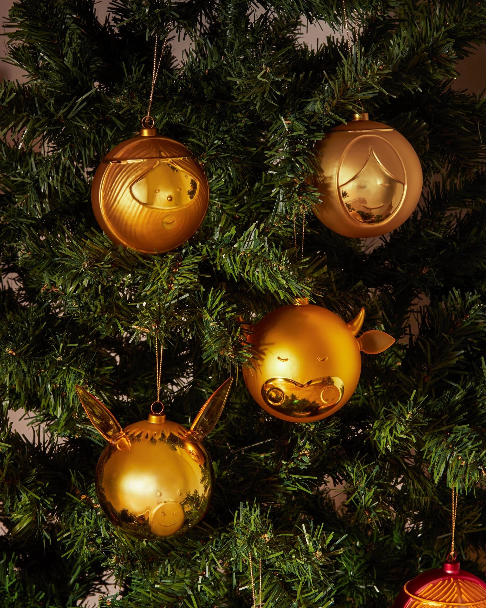 Golden cow-shaped ornament by Alessi, featuring subtle horns and a smiling face, on a green Christmas tree.