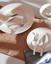 Shiny stainless steel cutlery by Alessi, with forks and knives on white plates and a woven placemat.
