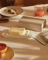Matte beige Mattina butter box by Alessi, on a white ceramic base with butter and a knife.