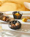 Three black metal decorative baskets by Alessi, with organic cut-out patterns, displayed with breadsticks, lemons, and bread rolls.