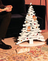 White stylized Christmas tree by Alessi, decorated with colorful ornaments and festive tags in a cozy living room.
