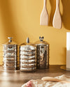 Silver metal Kalistò 2 jars by Alessi, each with a distinctive lid handle, displayed on a counter.