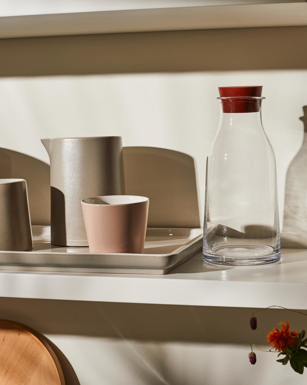 Matte beige ceramic pitcher by Alessi, a tall, simple design on a tray with two cups and a clear bottle.
