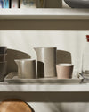 Muted ceramic tableware set by Alessi, with pitchers, cups, and a rectangular tray on a shelf.