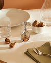 Silver-toned screw-press nutcracker by Alessi, holding a walnut on a dining table with cracked shells.