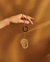 Gold pendant necklace with black ring by Alessi, featuring a textured circular pendant, held by a hand.