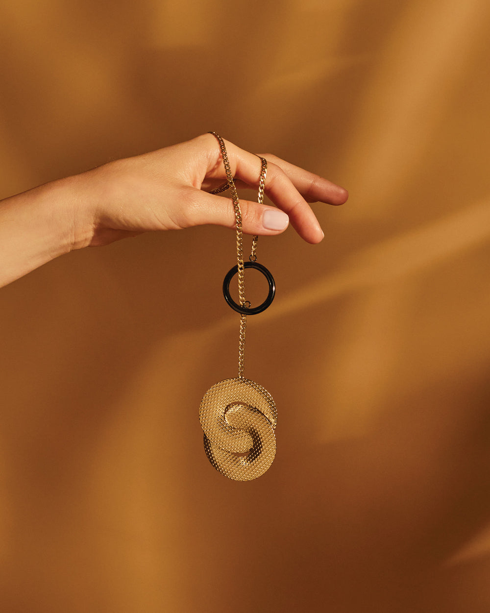 Gold pendant necklace with black ring by Alessi, featuring a textured circular pendant, held by a hand.