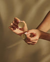 Golden perforated discs by Alessi, held in hands against a warm, shadowy background.