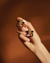 Geometric gold and black studded earrings by Alessi, held in a hand with light pink nails.