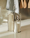 Silver-toned cup dispensers with a branch design by Alessi, holding beige disposable cups on a kitchen counter.