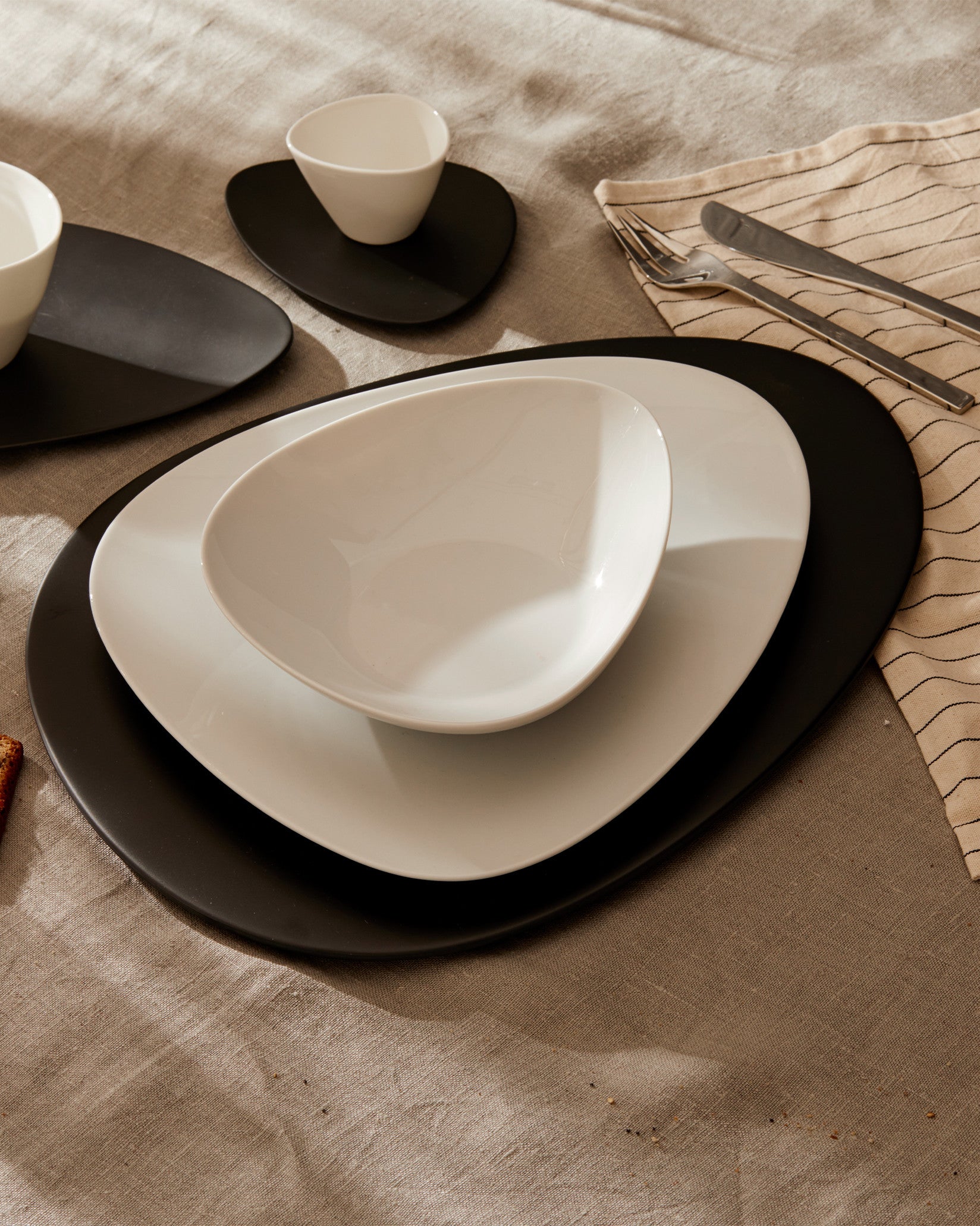Asymmetrical oval white and black dinnerware by Alessi, layered on a beige linen tablecloth.