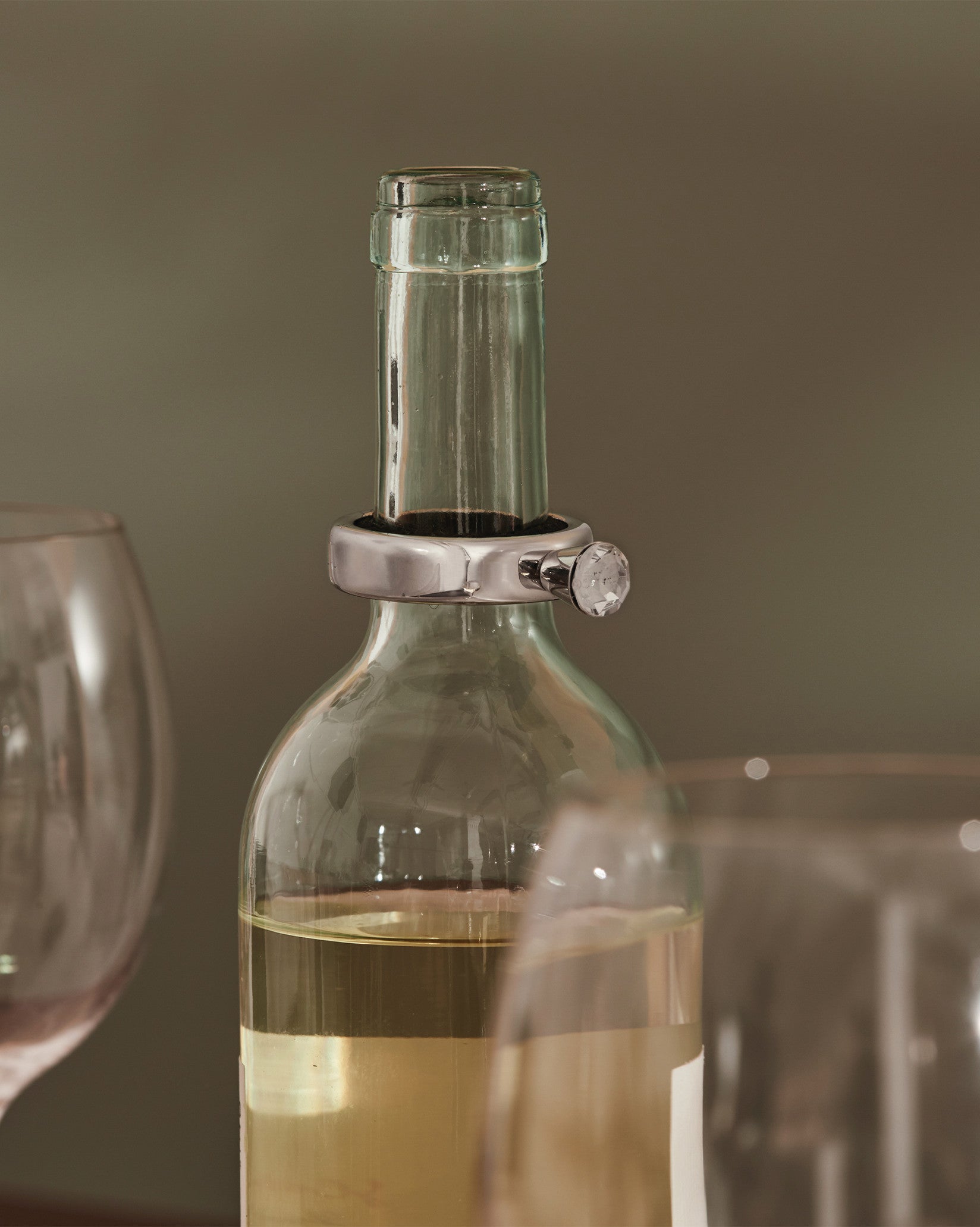Silver wine bottle collar by Alessi, featuring a clear faceted stone, on a white wine bottle.