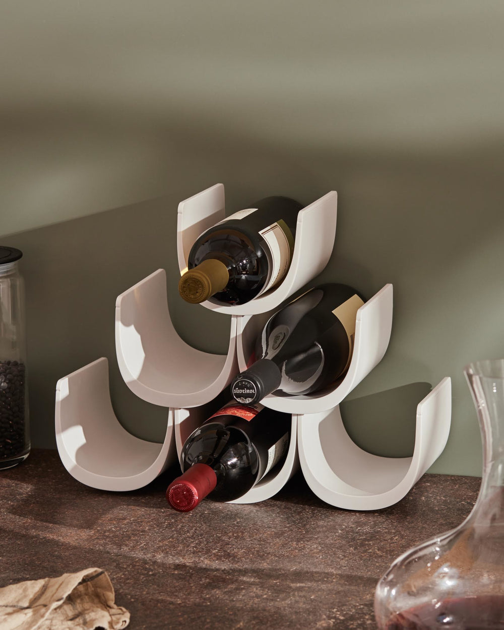 White modular wine rack by Alessi, holding three wine bottles on a speckled countertop.