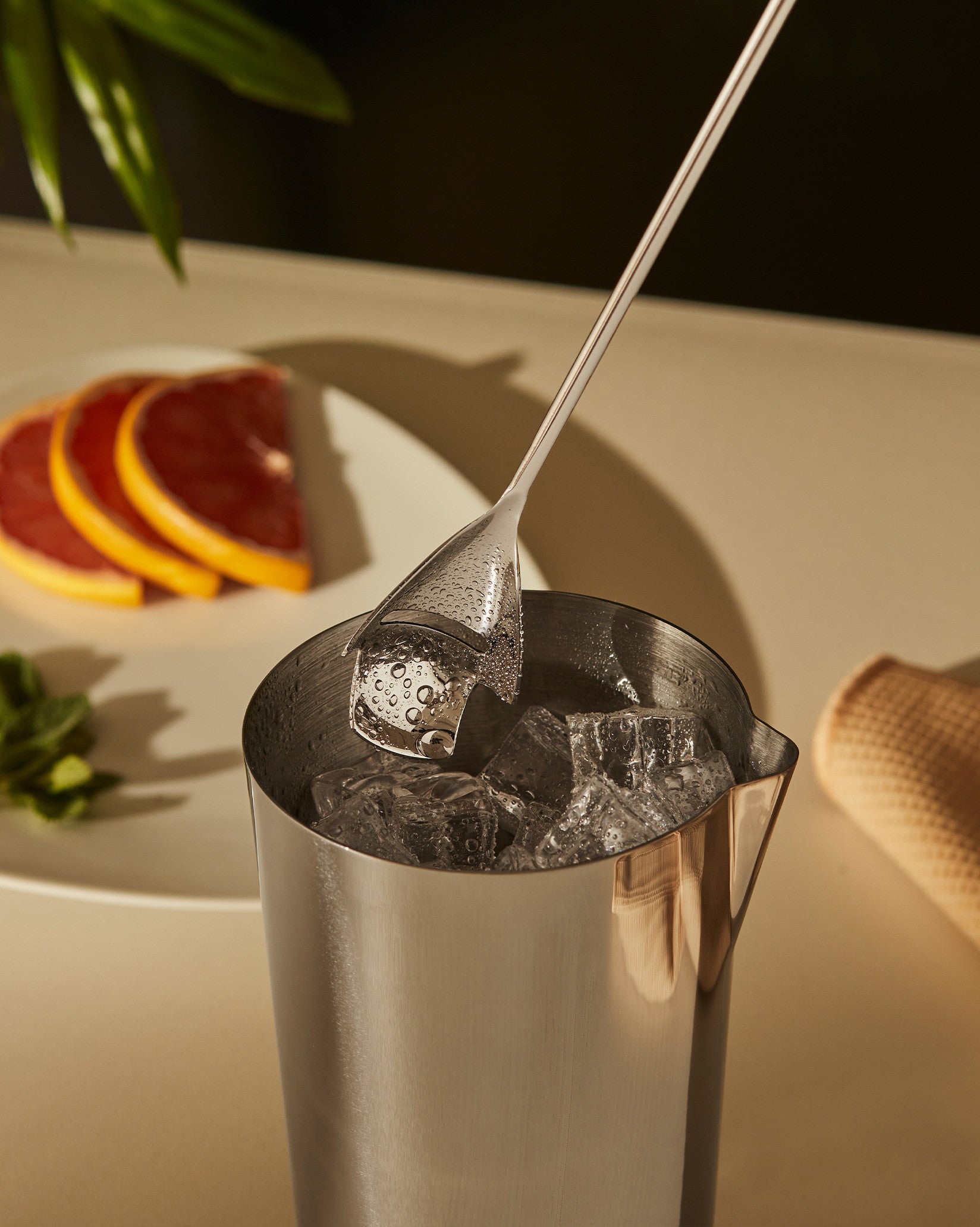 The tending box by Alessi, a stainless steel cocktail shaker with ice, a clear scoop, and grapefruit slices.