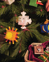 Orange Sunflake ornament by Alessi, a cuboid sun with a smiling face, hanging on a Christmas tree.