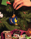 Blue and gold cube-shaped Mooncube ornament by Alessi, featuring crescent and full moon designs, being hung on a green Christmas tree.