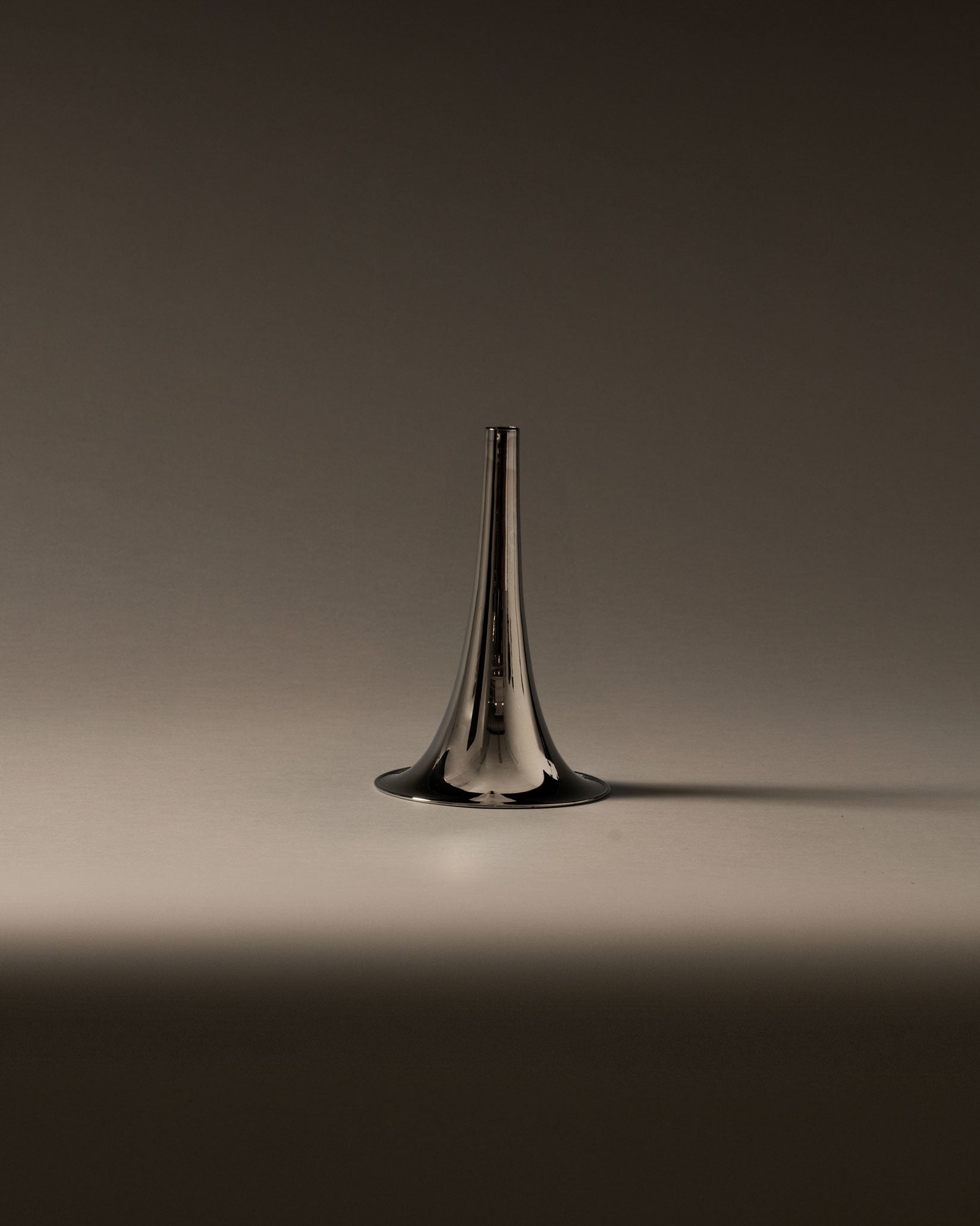 Silver metallic trumpet-shaped vase by Alessi, upright on a soft gradient background.
