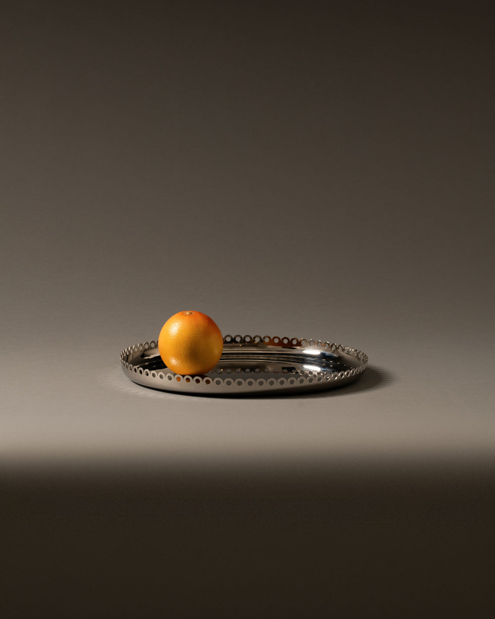 Oval silver metal fruit holder by Alessi with a perforated edge, holding a grapefruit.
