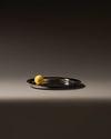 Silver oval metal tray by Alessi with a high-shine finish, featuring a single yellow sphere.