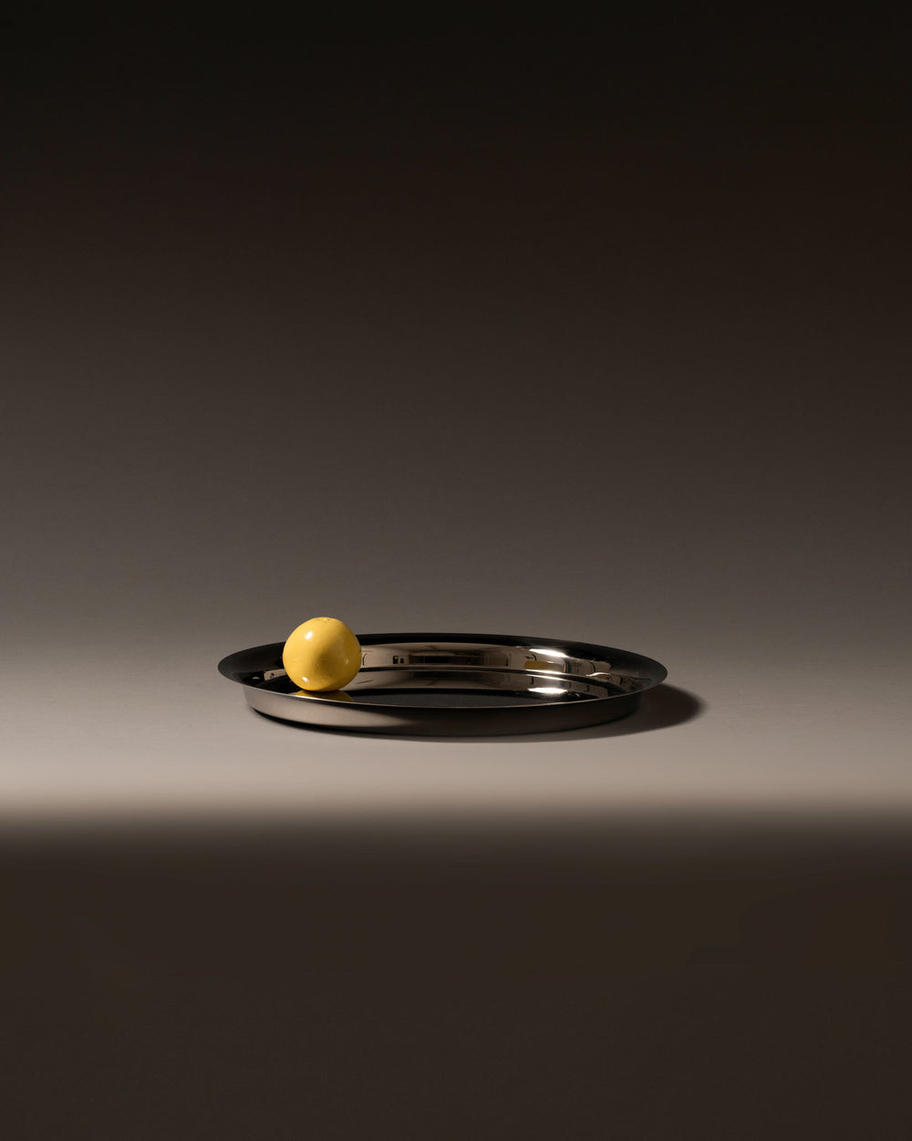 Silver oval metal tray by Alessi with a high-shine finish, featuring a single yellow sphere.