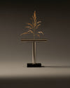 T-shaped metallic vase by Alessi on a black base, holding a dried golden plant.