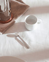 Silver moka pot by Alessi, with a copper base, on a linen napkin next to a white cup and spoon.