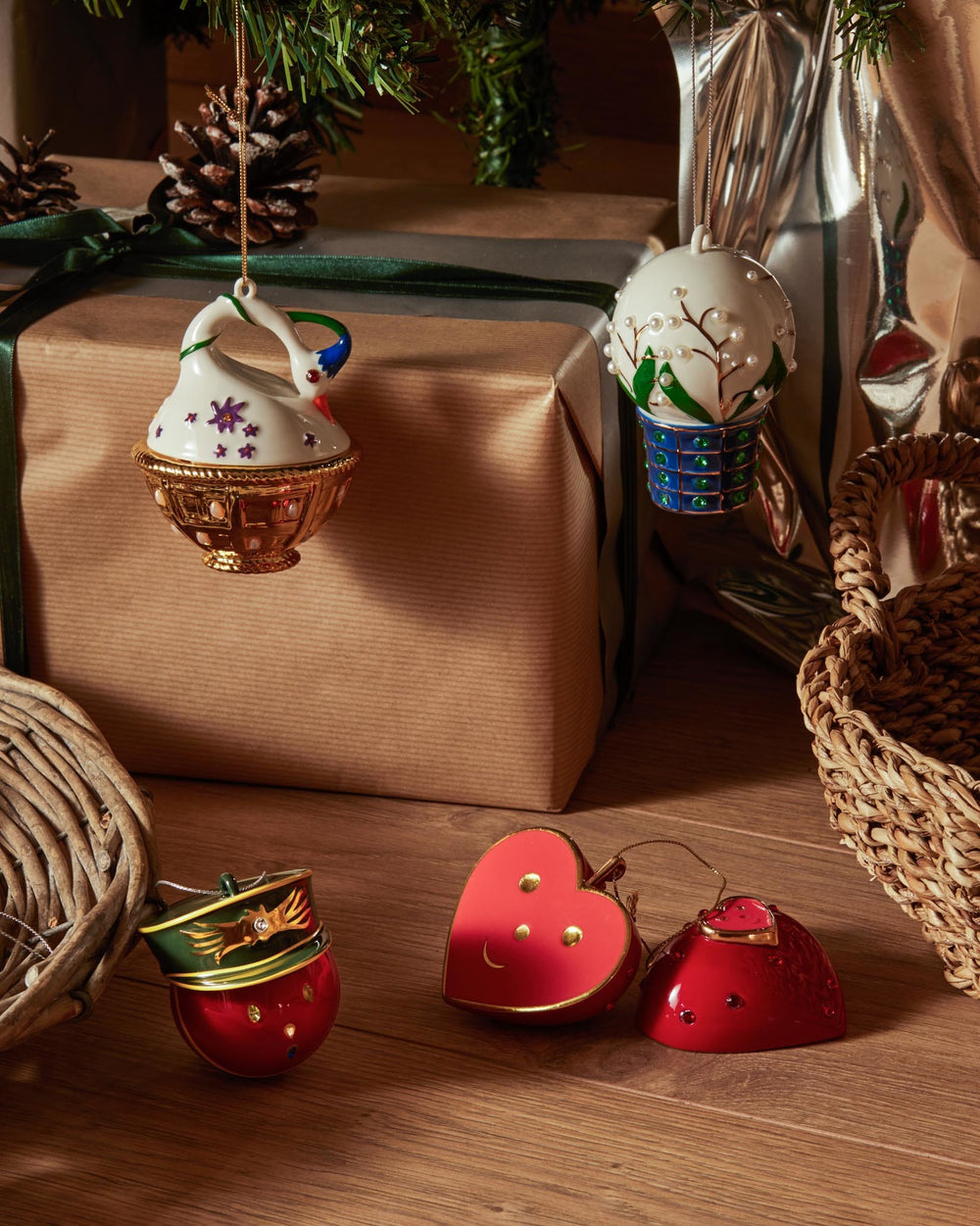 Red heart and bell-shaped ornaments by Alessi, with gold accents and jewel details, on a wooden floor.