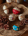 Red and white ladybug decorative ornament by Alessi, adorned with rhinestones, in a woven basket with other ornaments and pinecones.