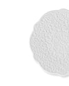 White ceramic plate by Alessi with a raised baroque pattern and scalloped edge, partially visible.