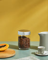 Clear glass storage jar by Alessi with a decorative silver patterned lid, holding dark granola.
