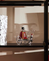 Silver and red Ringleader decorative figure by Alessi, wearing a top hat and driving a wheeled carriage with a small companion.