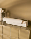 White cylindrical cotton pad dispenser by Alessi, open and filled with cotton pads on a beige tiled counter.