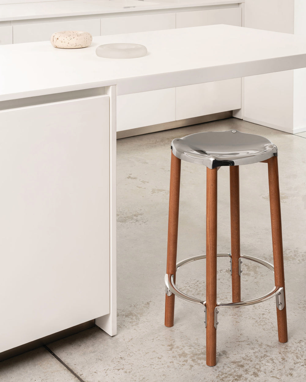 Wooden bar stool by Alessi with a polished silver seat and footrest, in a bright modern kitchen.