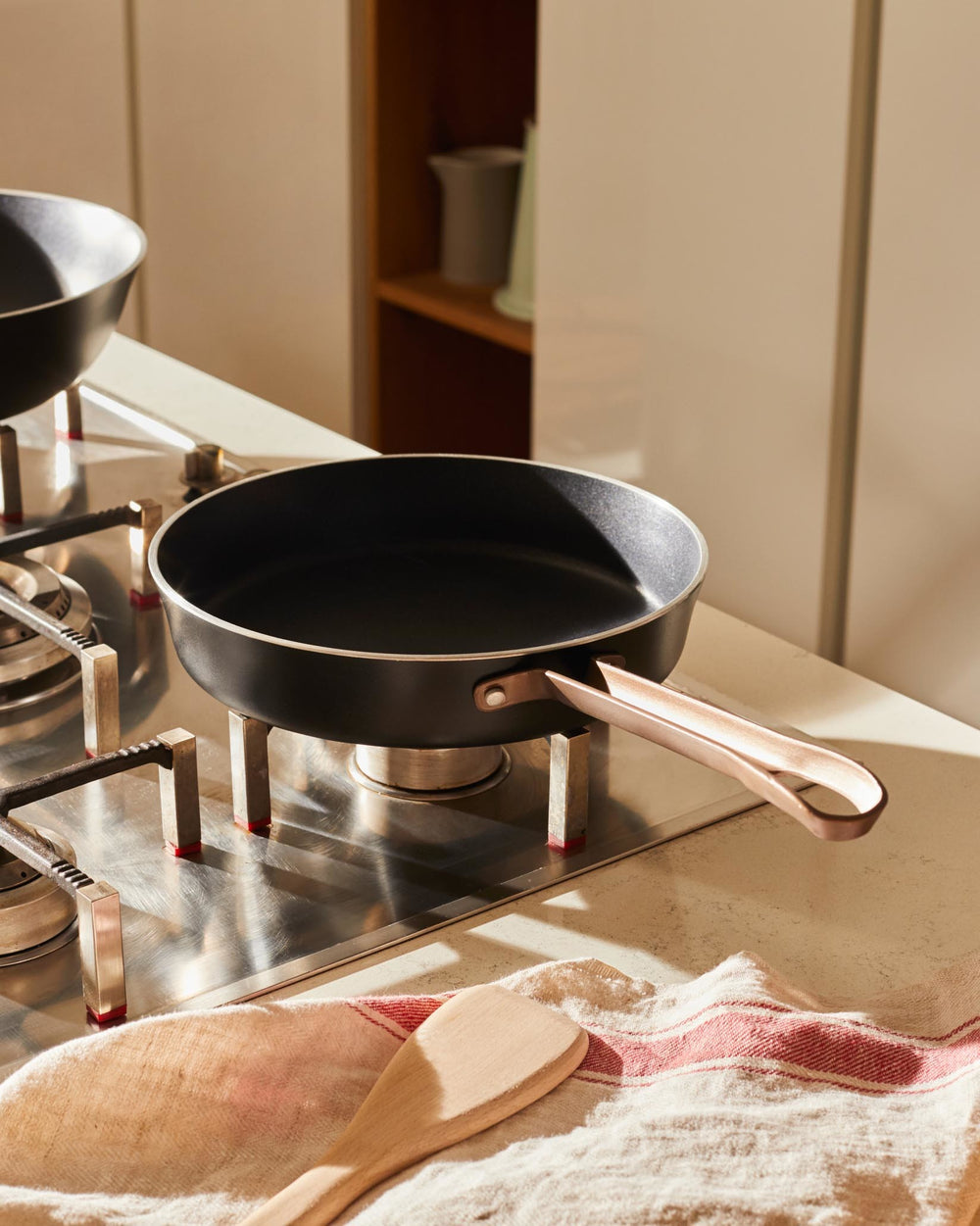 Black frying pan with rose gold handle by Alessi, resting on a stainless steel stovetop in a sunlit kitchen.