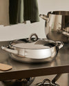 Stainless steel casserole by Alessi with a shiny finish, matching lid, and elegant oval handles.